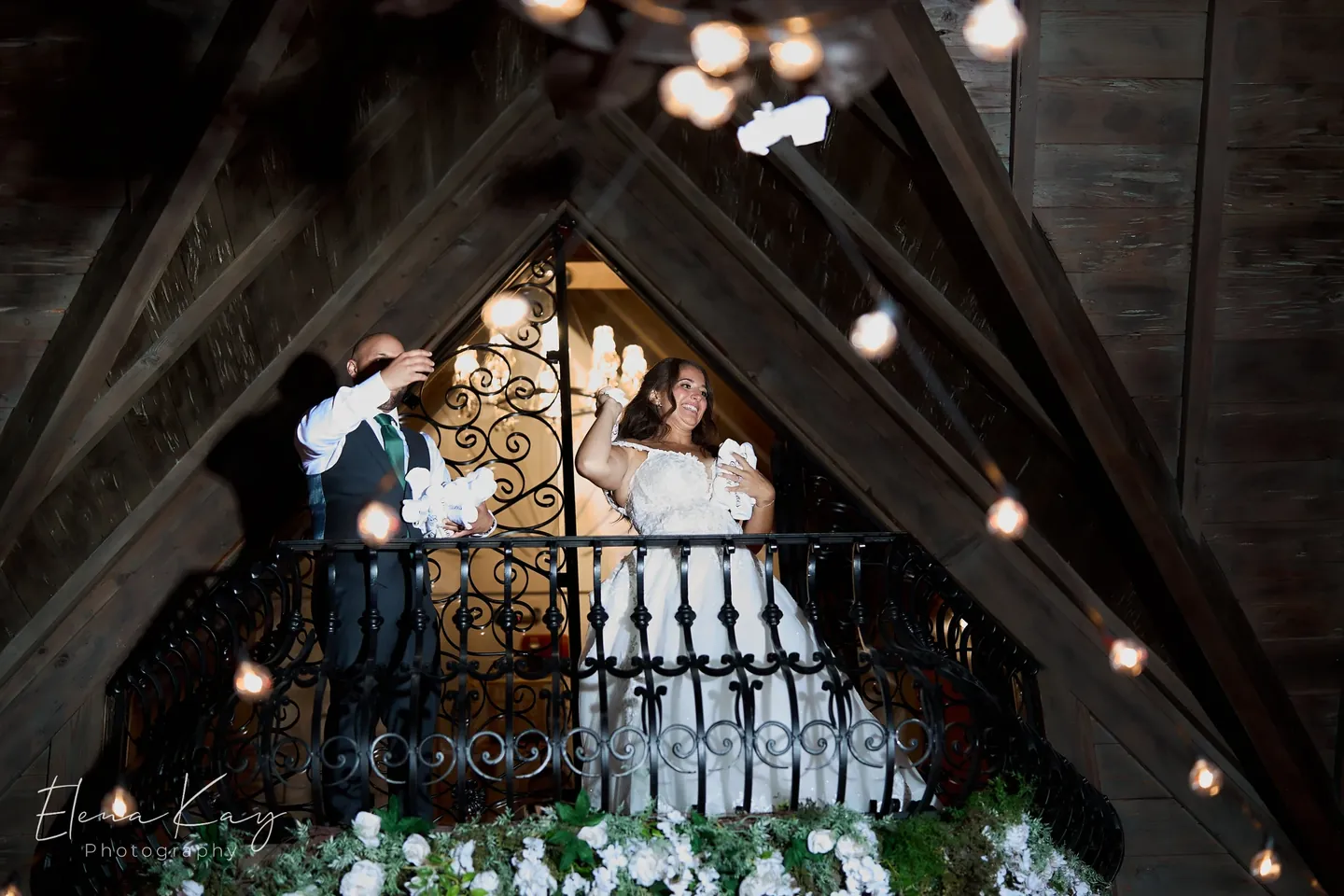 Bride and groom waving from the interior balcony overlooking the ballroom by Elena Kay Photography