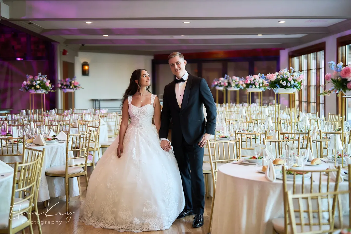 Bride and groom standing in the grand ballroom set with gold chairs and white linens by Elena Kay Photography